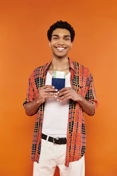 Alegre joven afroamericano en traje vívido con pasaporte y boleto y sonriendo a la cámara - foto de stock