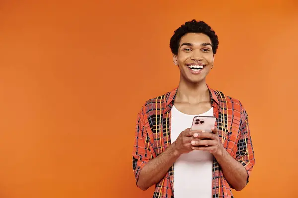 Good looking joyous african american man in vibrant outfit holding smartphone and looking at camera — Stock Photo