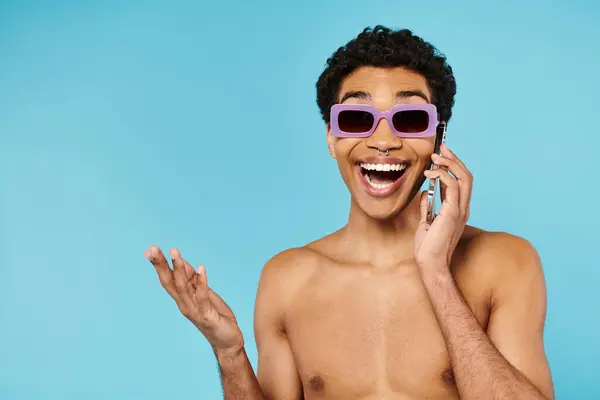 Feliz hombre afroamericano bien parecido en bañadores con gafas de sol con estilo hablando por teléfono - foto de stock