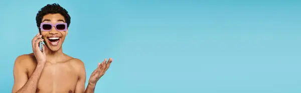 Alegre joven afroamericano hombre en traje de baño con gafas de sol con estilo hablando por teléfono, pancarta — Stock Photo