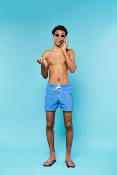 Jolly buen aspecto afroamericano hombre en bañador troncos con gafas de sol con estilo hablando por teléfono - foto de stock