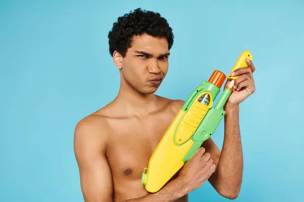 Bell'aspetto giovane uomo afro-americano in posa con pistola ad acqua e guardando la fotocamera sullo sfondo blu — Foto stock