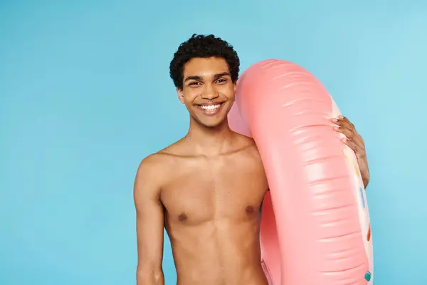 Homme afro-américain joyeux posant avec anneau de natation sur fond bleu et regardant la caméra — Photo de stock
