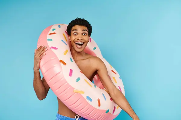 Homme afro-américain optimiste posant avec anneau de natation sur fond bleu et regardant la caméra — Photo de stock