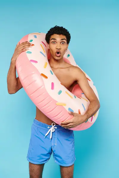 Homme afro-américain satisfait posant avec anneau de natation sur fond bleu et regardant la caméra — Photo de stock