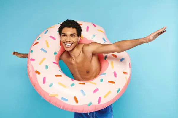 Hombre afroamericano positivo posando con anillo de natación sobre fondo azul y mirando a la cámara - foto de stock