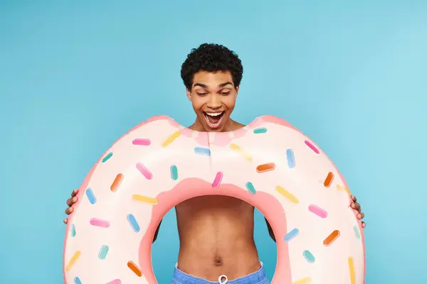 Lustige attraktive afrikanisch-amerikanische Mann vorgibt, aufblasbare Donut auf blauem Hintergrund essen — Stockfoto