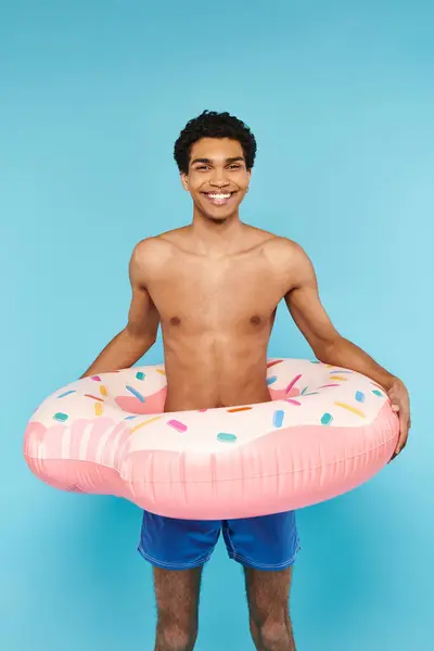 Schöner fröhlicher afrikanisch-amerikanischer Mann mit Schwimmring vor blauem Hintergrund, der in die Kamera schaut — Stockfoto