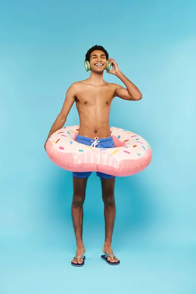 Homme afro-américain joyeux dans les troncs de natation avec beignet gonflable profiter de la musique dans les écouteurs — Photo de stock