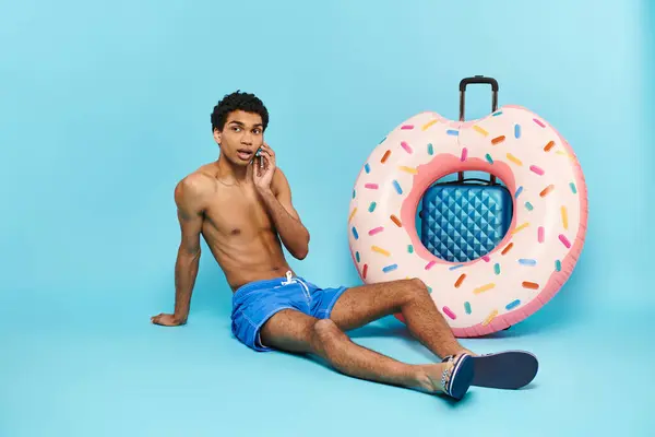 Young african american man talking by mobile phone next to his suitcase and inflatable donut — Stock Photo