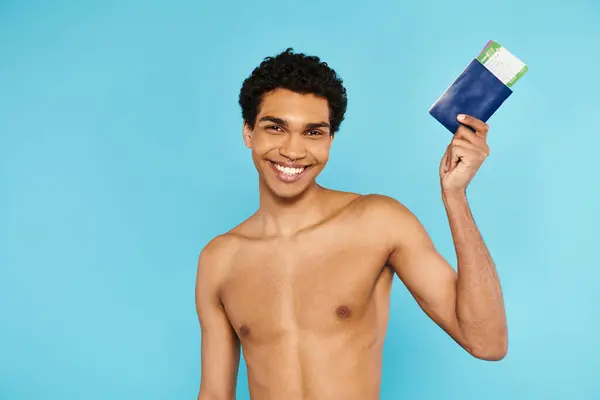 Alegre afroamericano hombre sosteniendo su pasaporte y billete sobre fondo azul y mirando a la cámara — Stock Photo