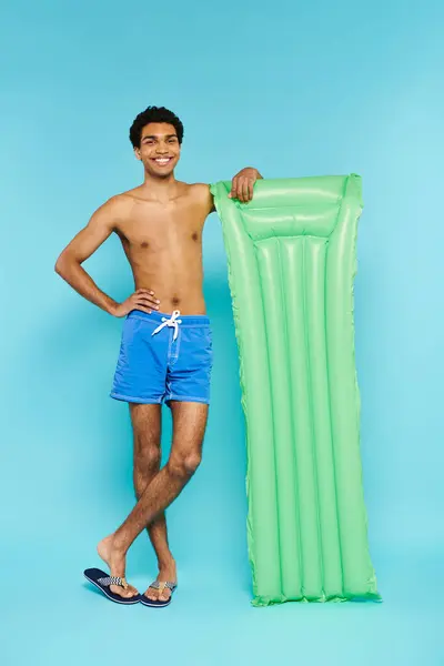 Positive african american man in swimming trunks posing with air mattress and smiling at camera — Stock Photo