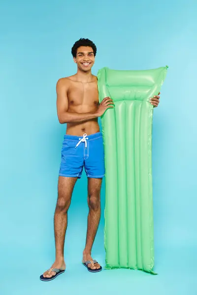 Gioioso uomo afroamericano in costume da bagno in posa con materasso ad aria e sorridente alla macchina fotografica — Foto stock