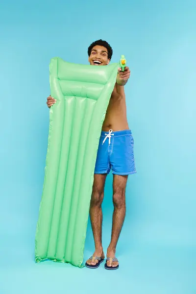 Joyful young african american man posing with air mattress and water gun on blue background — Stock Photo