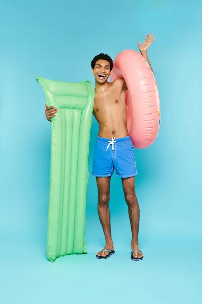 Alegre afroamericano hombre posando con colchón de aire y donut inflable y sonriendo a la cámara - foto de stock