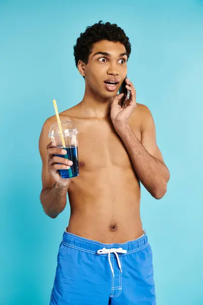 Hombre afroamericano guapo hablando por teléfono y sosteniendo refrescante cóctel en su mano - foto de stock