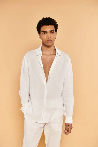 Appealing young african american man in white attire posing on beige backdrop and looking at camera — Stock Photo