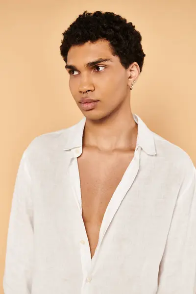 Hombre afro americano elegante y bien parecido en ropa blanca elegante mirando hacia otro lado en fondo beige - foto de stock