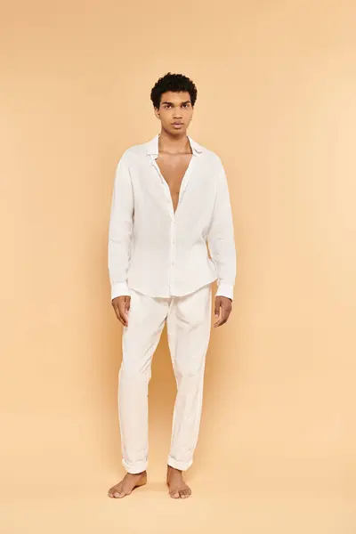 Alluring young african american man in white attire posing on beige backdrop and looking at camera — Stock Photo