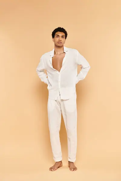 Atractivo joven afroamericano hombre en traje blanco posando sobre fondo beige y mirando a la cámara - foto de stock
