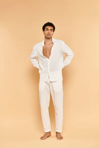 Attractive young african american man in white attire posing on beige backdrop and looking at camera — Stock Photo