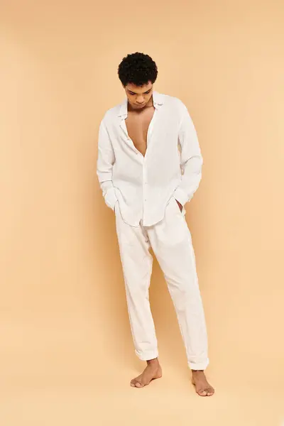 Elegante hombre afroamericano chic en ropa blanca elegante mirando hacia otro lado en fondo beige - foto de stock