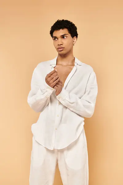 Guapo chic africano americano hombre en elegante ropa blanca mirando hacia otro lado en beige telón de fondo - foto de stock