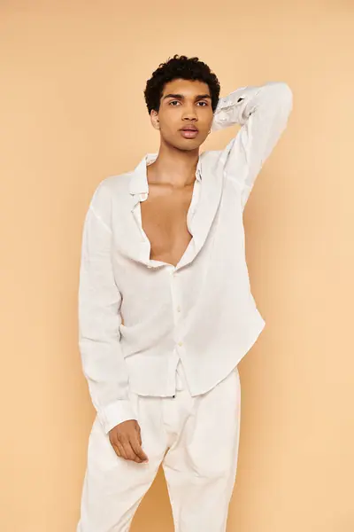 Hombre afroamericano con estilo en traje blanco posando sobre fondo beige y mirando a la cámara - foto de stock
