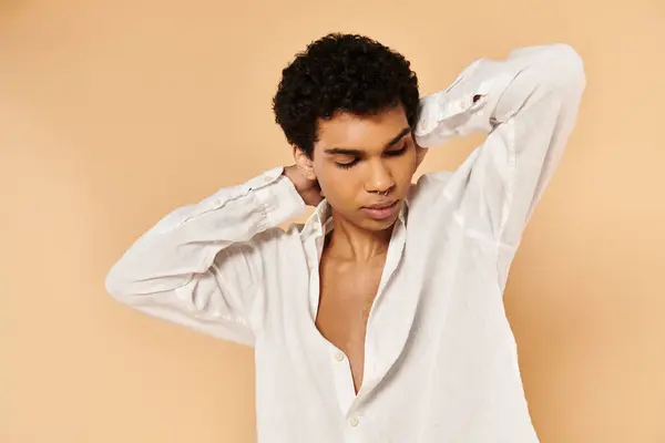 Atractivo hombre afroamericano elegante en ropa blanca elegante mirando hacia otro lado en fondo beige - foto de stock