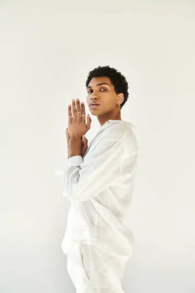 Exquisito joven afroamericano en traje blanco y mirando a la cámara en el fondo beige - foto de stock