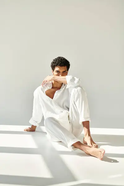 Appealing sophisticated african american man in linen attire sitting on floor and looking at camera — Stock Photo