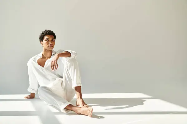 Guapo sofisticado afroamericano hombre en traje de lino sentado en el suelo y mirando a la cámara - foto de stock