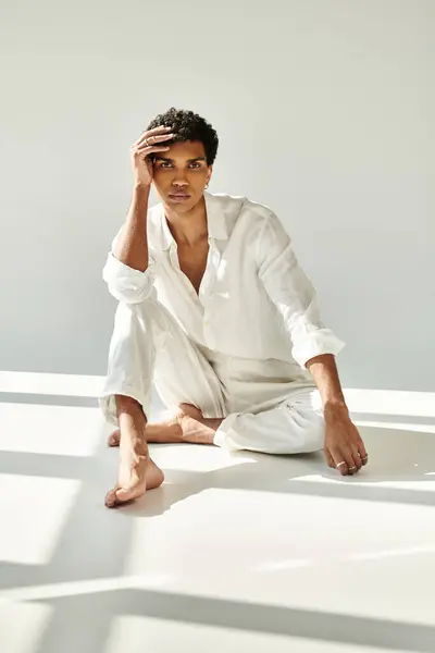 Exquisite young african american man in linen attire looking at camera on floor on beige backdrop — Stock Photo