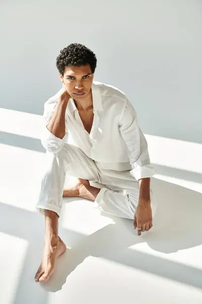 Elegant young african american man in linen attire looking at camera on floor on beige backdrop — Stock Photo