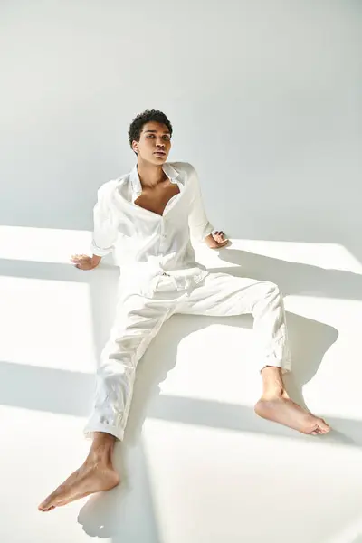 Fashionable african american man in linen attire looking at camera on floor on beige backdrop — Stock Photo