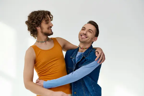 Good looking cheerfull lgbtq friends in vibrant clothes hugging on gray backdrop, pride month — Stock Photo