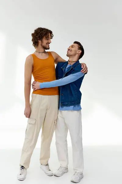Good looking positive lgbtq friends in vibrant clothes hugging on gray backdrop, pride month — Stock Photo