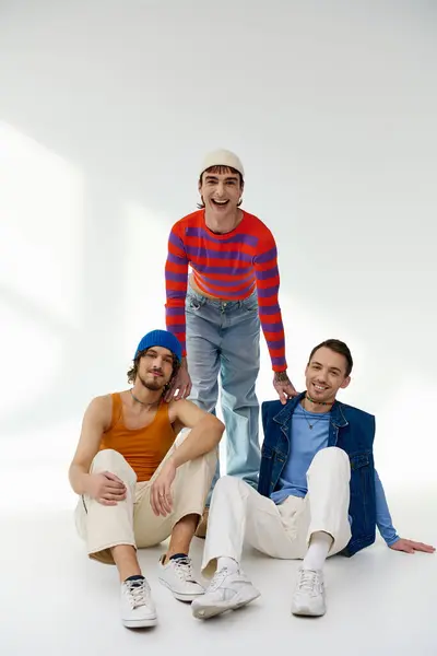 Alegre lgbtq amigos en vibrantes trajes posando juntos en gris telón de fondo y sonriendo a la cámara - foto de stock