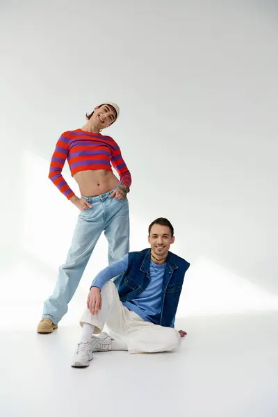 Два веселых привлекательных друга в ярких одеждах смотрят в камеру и позируют на сером фоне — стоковое фото