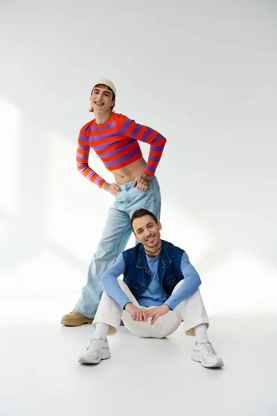 Two merry trendy lgbt friends in vibrant attires looking at camera and posing on gray backdrop — Stock Photo