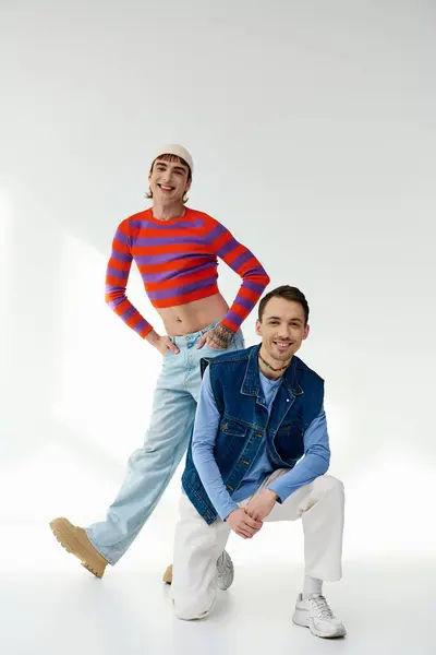 Two jolly stylish lgbt friends in vibrant attires looking at camera and posing on gray backdrop — Stock Photo