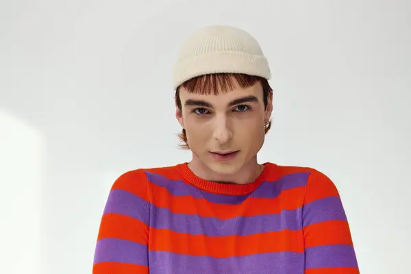 Positive trendy gay man with white hat in vivid attire posing on gray backdrop and looking at camera — Stock Photo