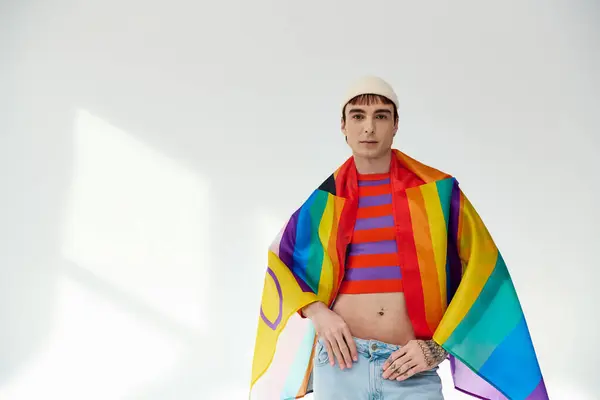 Веселый красивый гей в ярком наряде в белой шляпе с радужным флагом и смотрящий в камеру — стоковое фото