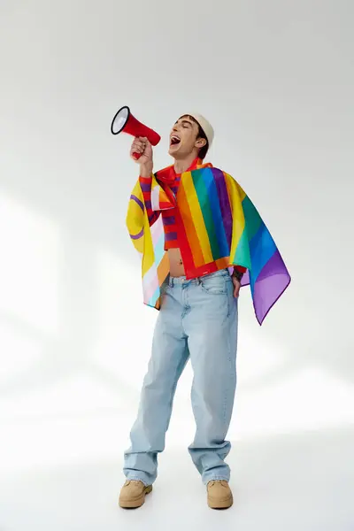 Cheerful stylish gay man in vibrant attire with rainbow flag using megaphone and looking away — Stock Photo