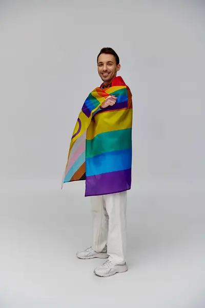 Alegre atractivo gay hombre en vibrante casual atuendo sosteniendo arco iris bandera y sonriendo a cámara - foto de stock