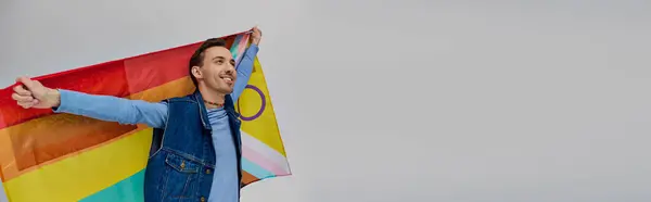 Alegre guapo gay hombre en moderno traje sosteniendo arco iris bandera y mirando lejos, orgullo mes, bandera - foto de stock