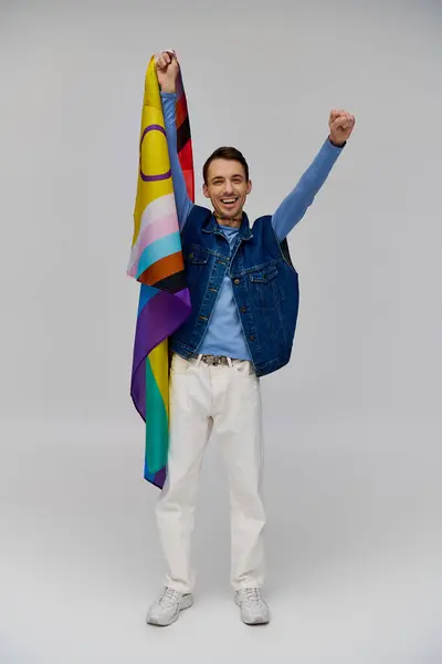 Feliz bom olhar gay homem em vibrante casual traje segurando arco-íris bandeira e sorrindo para a câmera — Fotografia de Stock