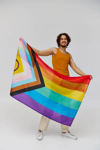 Positive alluring gay man with dark hair holding rainbow flag and smiling happily at camera — Stock Photo