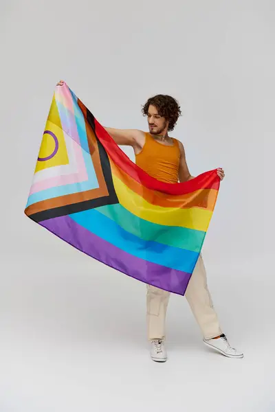 Alegre joven gay hombre con oscuro cabello en vibrante traje posando con arco iris bandera y mirando hacia otro lado - foto de stock