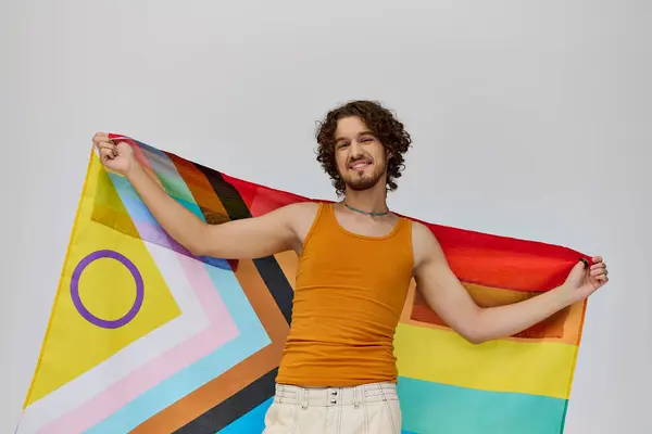 Contented alluring gay man with dark hair holding rainbow flag and smiling happily at camera — Stock Photo